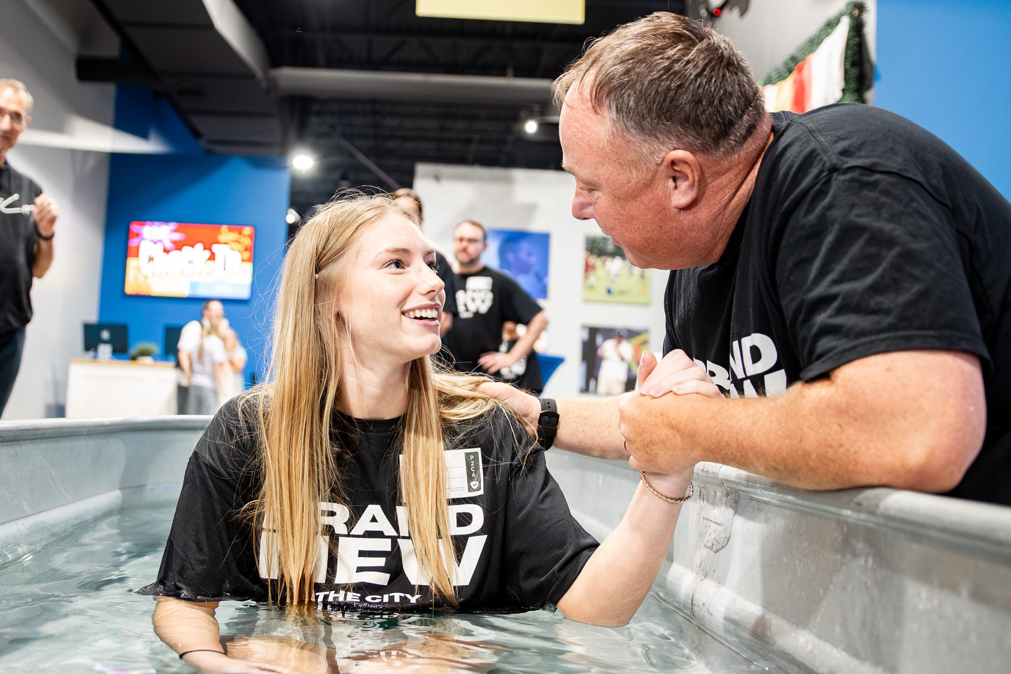 A smiling woman in the baptism tank, with a leader holding her hands